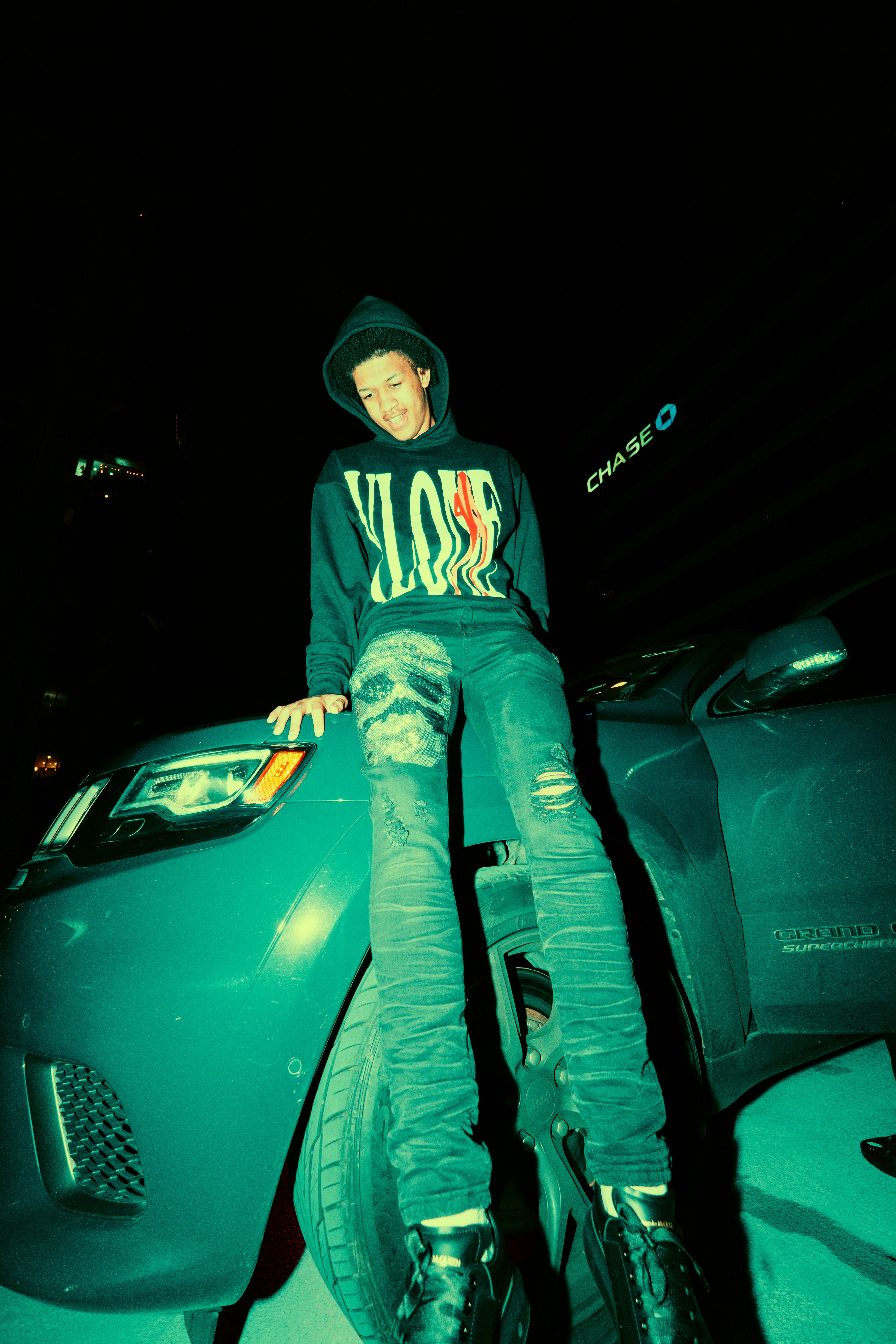 man in black and white hoodie and gray pants sitting on black car